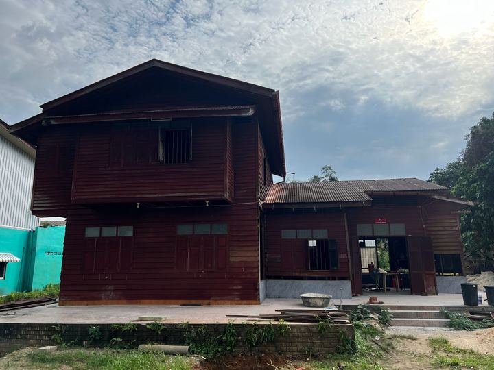 บ้านไม้ก่อนซ่อม ผนังสีแดงเข้ม หลังคาสังกะสี / The wooden house before repair, dark red walls and tin roof